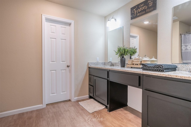 full bathroom featuring double vanity, a sink, baseboards, and wood finished floors