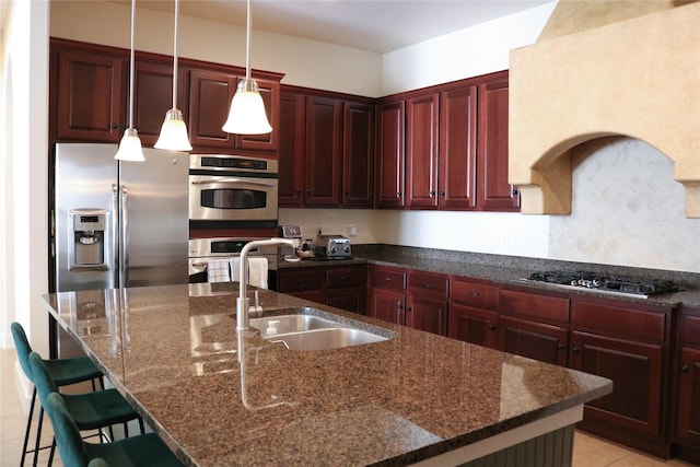 kitchen featuring reddish brown cabinets, stainless steel appliances, an island with sink, and a sink