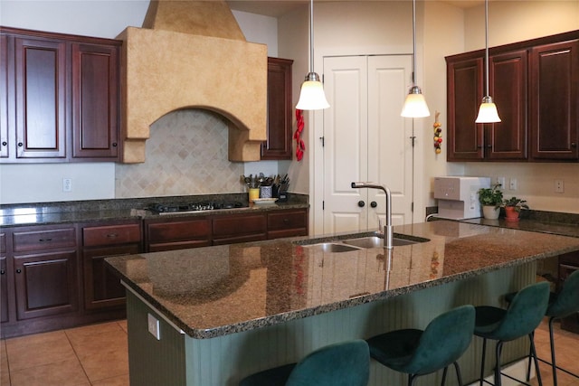 kitchen with black gas cooktop, tasteful backsplash, a sink, dark stone countertops, and a kitchen bar