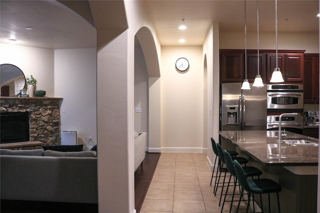 kitchen featuring stainless steel refrigerator with ice dispenser, a sink, a stone fireplace, dark stone countertops, and a kitchen bar