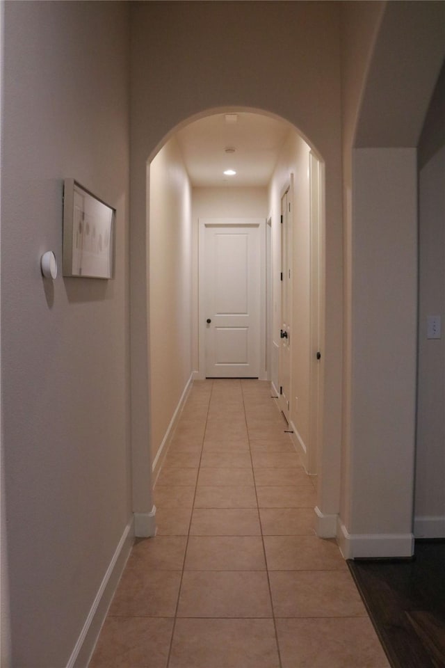 hall featuring light tile patterned floors, arched walkways, and baseboards