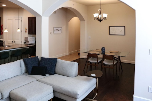 living area featuring arched walkways, dark wood-style flooring, an inviting chandelier, and baseboards