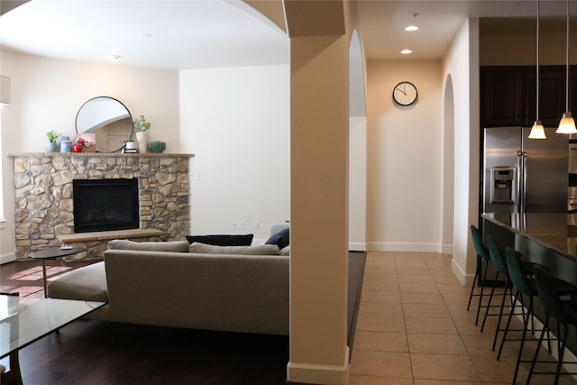 living room with recessed lighting, a stone fireplace, baseboards, and light tile patterned floors