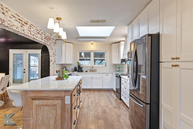 kitchen featuring a skylight, visible vents, electric range, freestanding refrigerator, and a sink