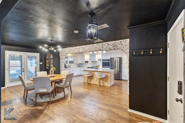 dining room featuring arched walkways, french doors, crown molding, light wood-style flooring, and a textured ceiling