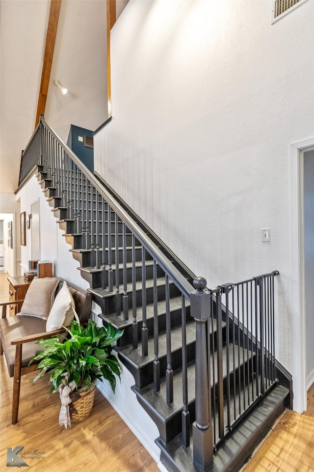 stairway featuring baseboards, visible vents, a towering ceiling, wood finished floors, and beamed ceiling