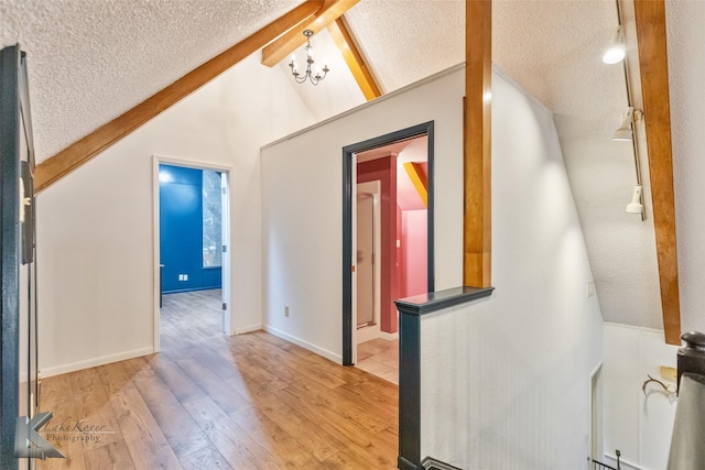 corridor with vaulted ceiling with beams, light wood finished floors, an inviting chandelier, a textured ceiling, and baseboards