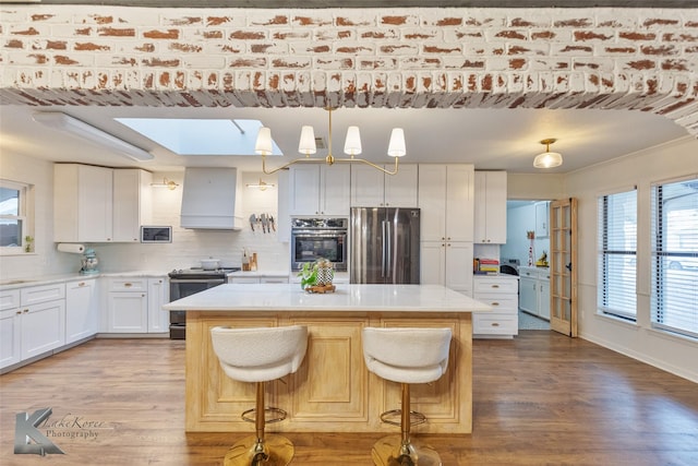 kitchen with stainless steel appliances, premium range hood, a skylight, wood finished floors, and a kitchen island