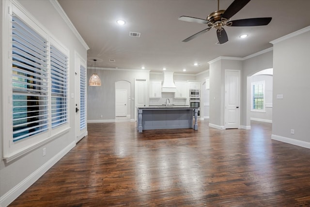 kitchen featuring arched walkways, custom range hood, visible vents, stainless steel microwave, and a sink