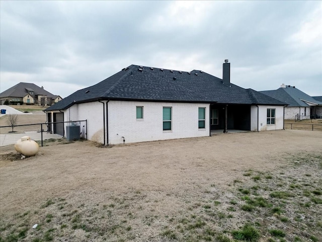 rear view of house with a chimney, roof with shingles, fence, central air condition unit, and brick siding