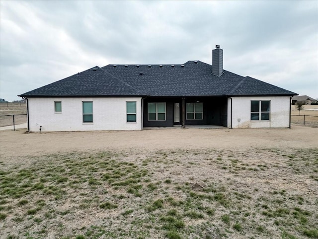 back of house featuring a shingled roof, a chimney, and fence