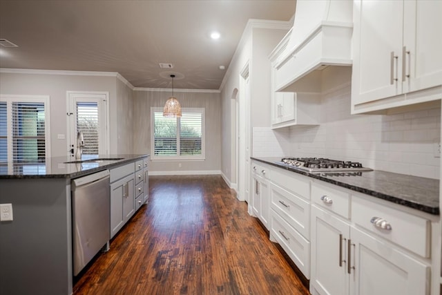 kitchen with dark wood-style flooring, custom exhaust hood, appliances with stainless steel finishes, ornamental molding, and dark stone counters