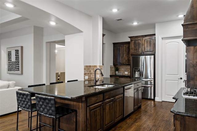 kitchen with dark wood-type flooring, a sink, appliances with stainless steel finishes, tasteful backsplash, and dark stone countertops