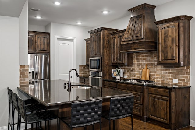 kitchen with a sink, a kitchen breakfast bar, appliances with stainless steel finishes, tasteful backsplash, and custom range hood