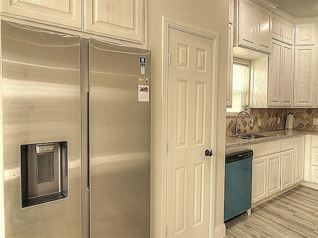 kitchen featuring light wood finished floors, backsplash, a sink, stainless steel fridge, and dishwashing machine