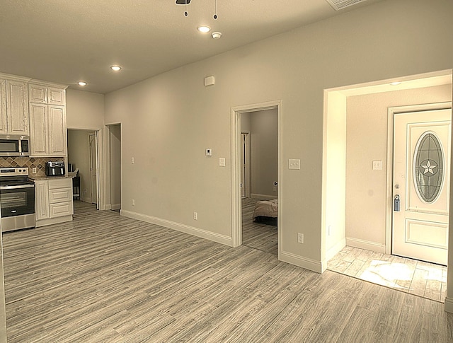 kitchen with baseboards, decorative backsplash, appliances with stainless steel finishes, light countertops, and light wood-type flooring