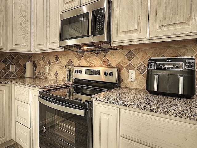 kitchen with appliances with stainless steel finishes, cream cabinets, dark countertops, and backsplash