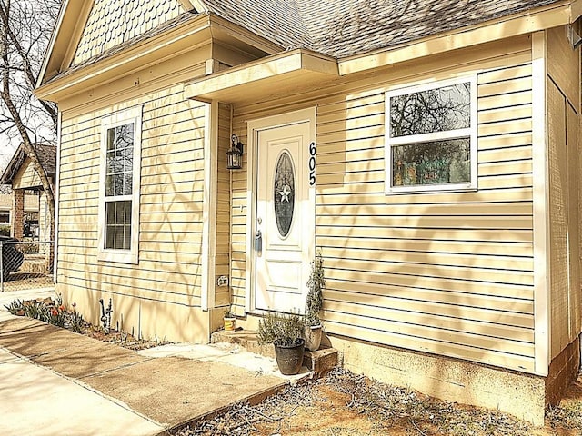 doorway to property featuring fence and roof with shingles