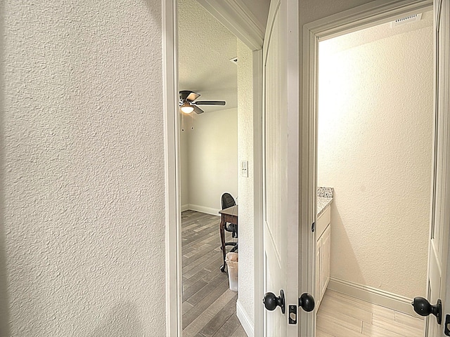 hallway with a textured ceiling, a textured wall, light wood-style flooring, and baseboards