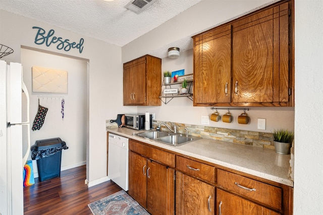 kitchen with visible vents, brown cabinetry, a sink, a textured ceiling, and white appliances