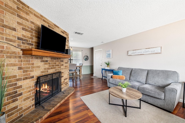 living room featuring dark wood-type flooring, a brick fireplace, visible vents, and a textured ceiling