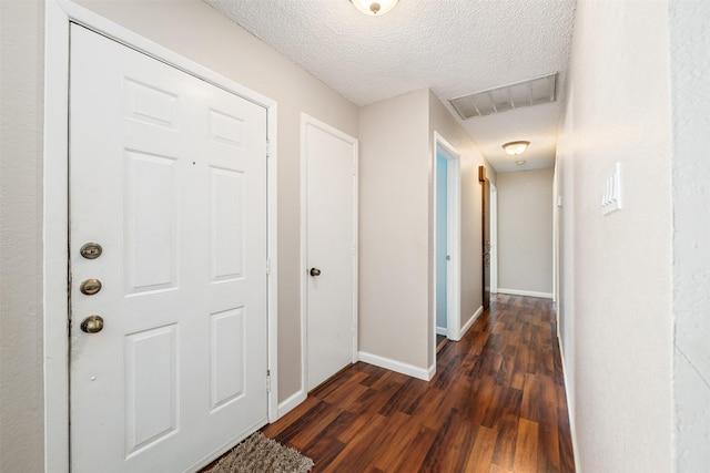 hallway featuring a textured ceiling, dark wood finished floors, visible vents, and baseboards