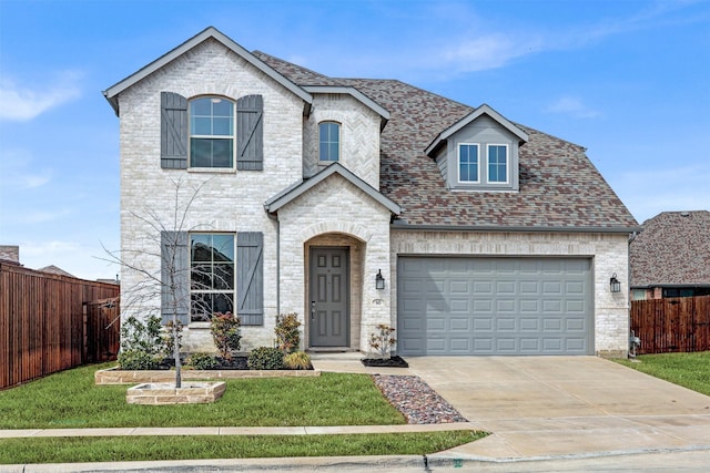 french country home with driveway, brick siding, and fence