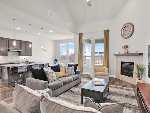 living area with baseboards, visible vents, a ceiling fan, a tile fireplace, and wood finished floors