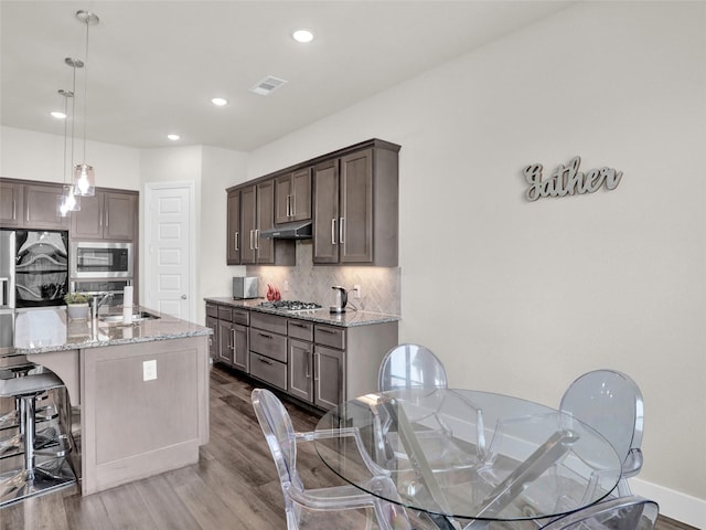 kitchen featuring visible vents, decorative backsplash, appliances with stainless steel finishes, light stone countertops, and under cabinet range hood