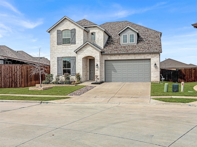 french provincial home featuring concrete driveway, brick siding, fence, and a front lawn