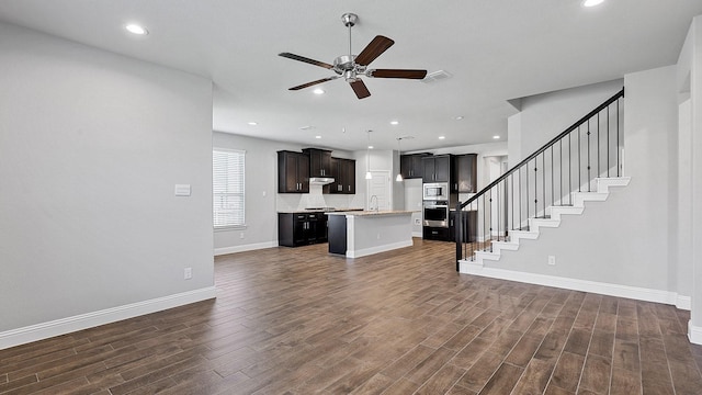 unfurnished living room with dark wood-type flooring, visible vents, a sink, and stairs