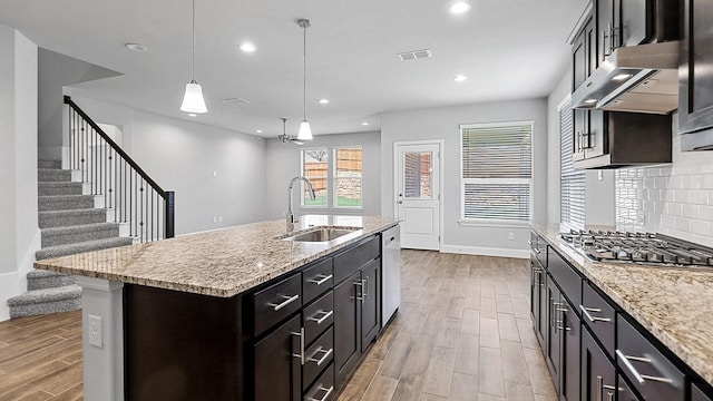 kitchen with under cabinet range hood, a sink, appliances with stainless steel finishes, decorative backsplash, and wood tiled floor