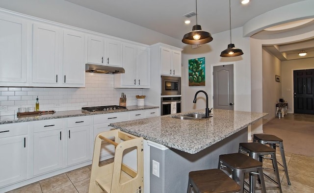 kitchen with light stone countertops, under cabinet range hood, stainless steel appliances, a sink, and decorative backsplash