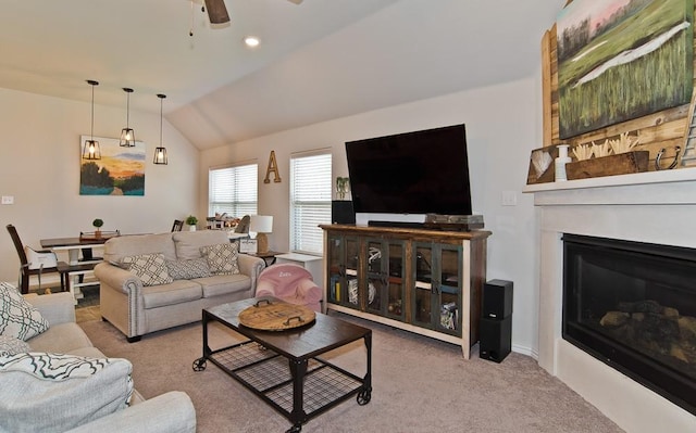 living room with vaulted ceiling, carpet, a glass covered fireplace, and a ceiling fan