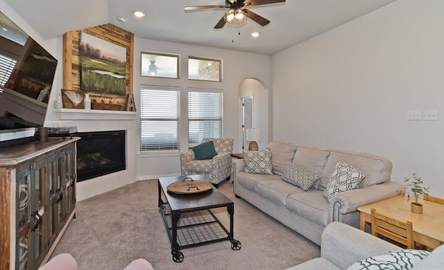 carpeted living room featuring a ceiling fan, arched walkways, a large fireplace, and recessed lighting