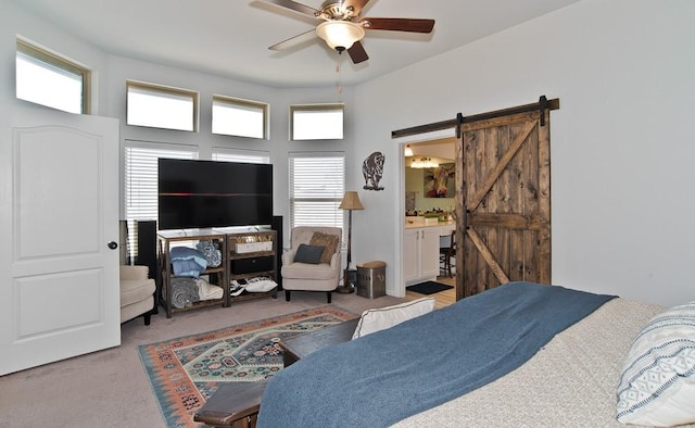 bedroom with carpet floors, a barn door, connected bathroom, and a ceiling fan