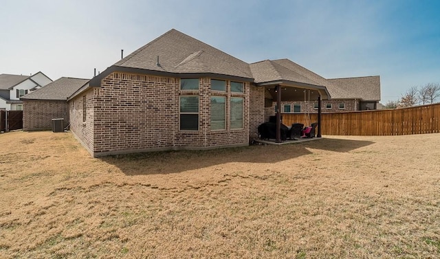 back of property with a yard, brick siding, fence, and central AC