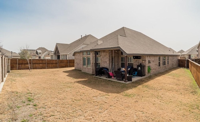 rear view of house with a yard, brick siding, a patio, and a fenced backyard