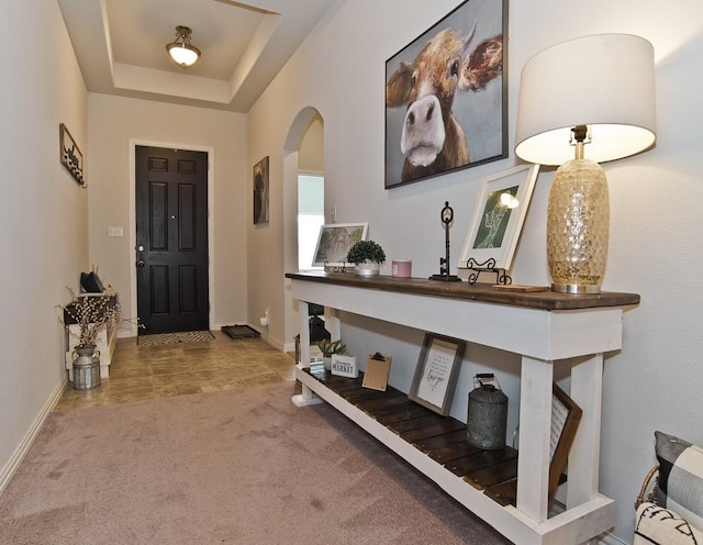 carpeted foyer entrance featuring baseboards, arched walkways, and a raised ceiling