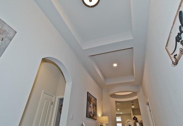 corridor with arched walkways, a tray ceiling, and recessed lighting