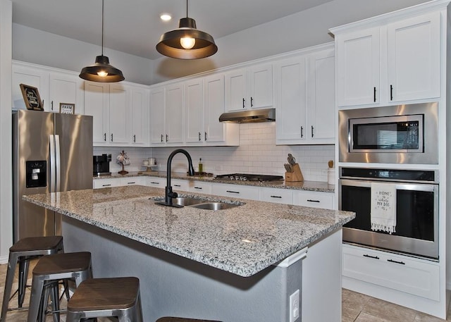 kitchen with stainless steel appliances, backsplash, a sink, under cabinet range hood, and a kitchen bar