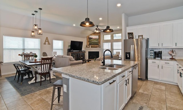 kitchen featuring a fireplace, stainless steel appliances, tasteful backsplash, a kitchen island with sink, and a sink