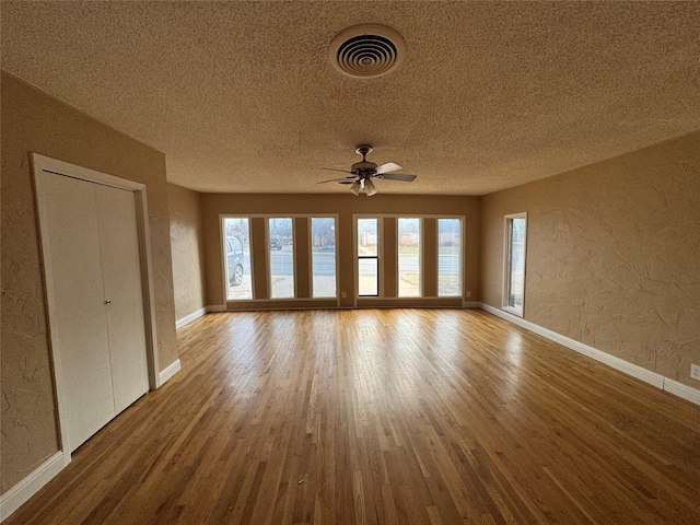 empty room with visible vents, a textured wall, a textured ceiling, and wood finished floors