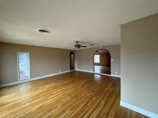 empty room featuring arched walkways, visible vents, a textured wall, a textured ceiling, and wood finished floors