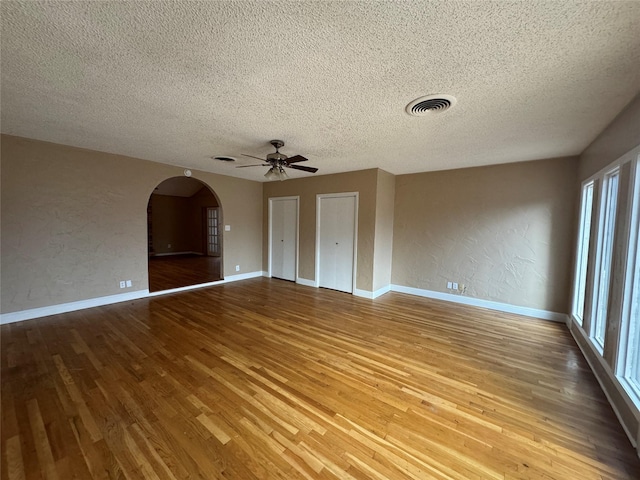 spare room with arched walkways, a textured wall, wood finished floors, and visible vents