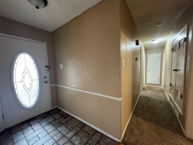 entryway featuring stone tile flooring, a textured wall, a textured ceiling, and baseboards