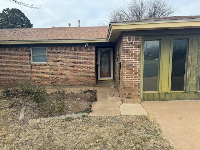 view of exterior entry with brick siding and roof with shingles