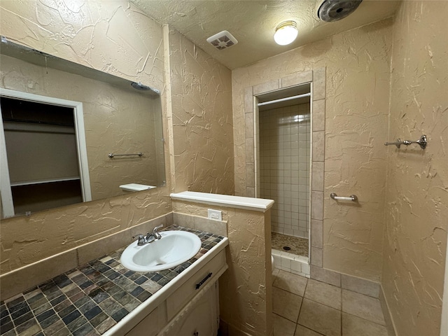 bathroom with visible vents, a textured wall, a textured ceiling, and tiled shower