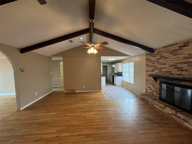 unfurnished living room with light wood-type flooring, vaulted ceiling with beams, a fireplace, and a textured ceiling