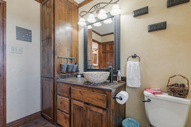 half bathroom with a textured wall, toilet, ornamental molding, vanity, and baseboards